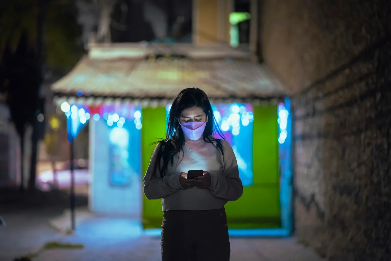 Mujer revisando su celular de noche en una calle iluminada